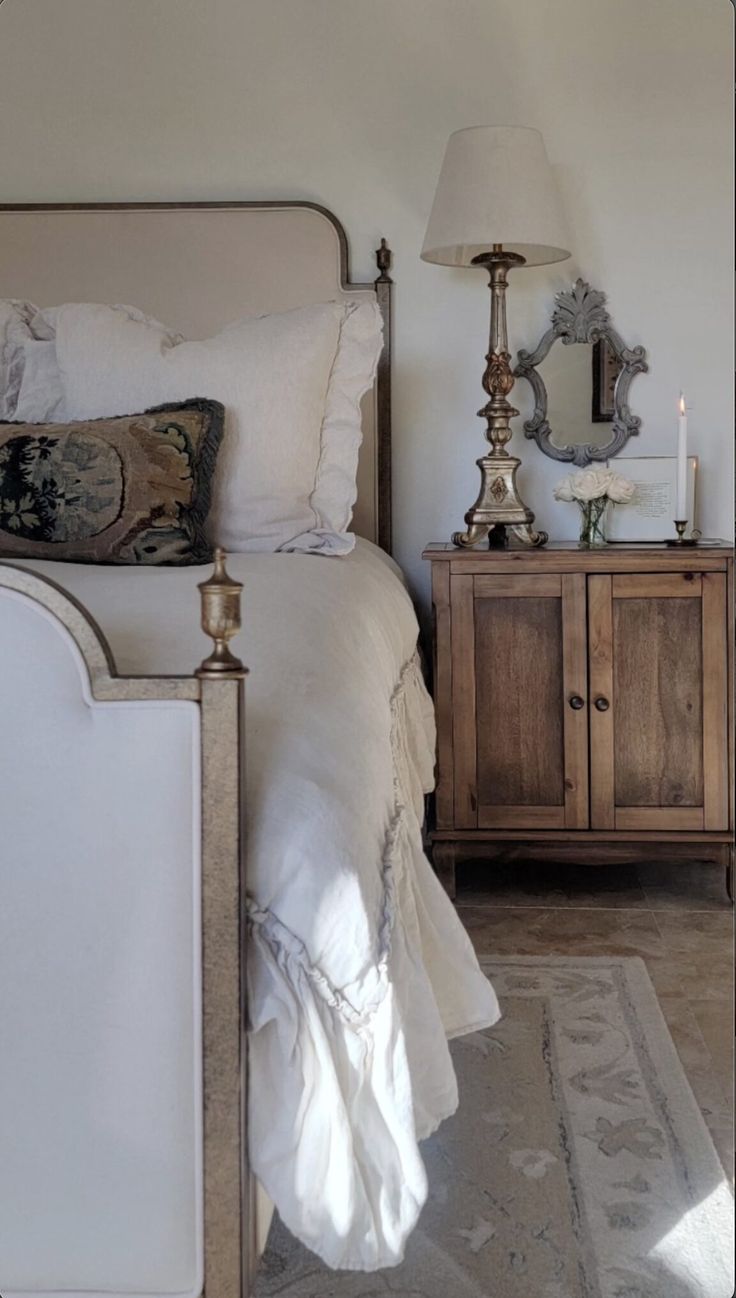 a white bed sitting next to a wooden dresser with a lamp on top of it