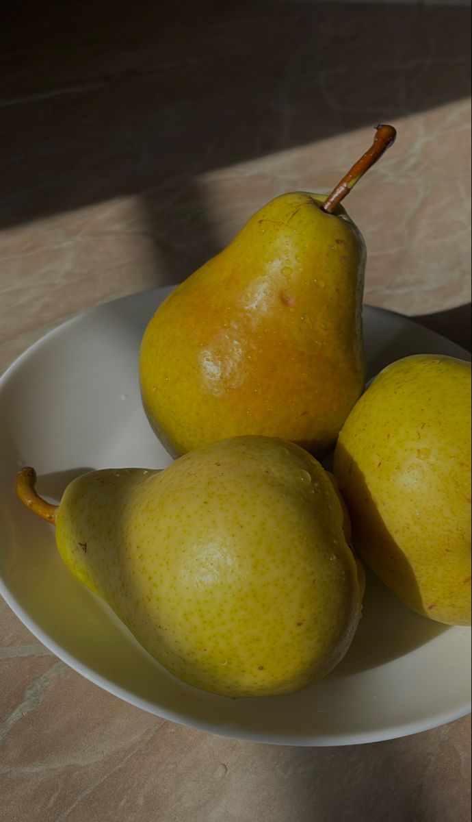 three pears in a white bowl on a table