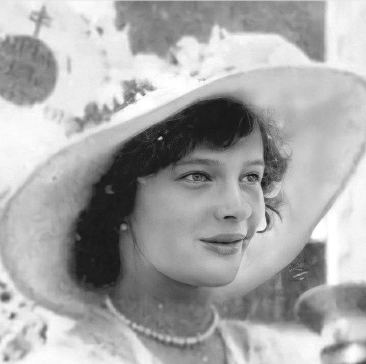 a woman wearing a white hat and pearls on her neck, looking at the camera