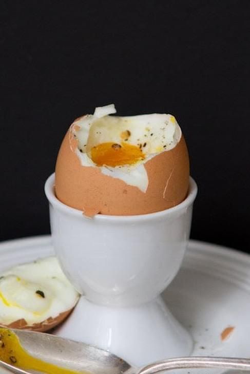 an egg is broken in half on a white plate with a fork and spoon next to it