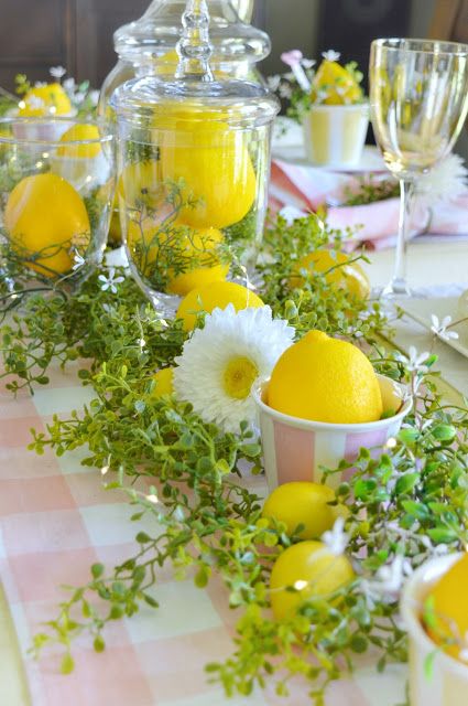 the table is set with lemons, daisies and greenery in glass jars