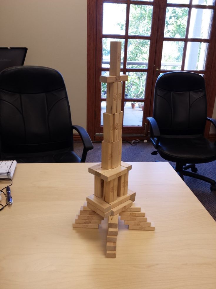 a wooden tower sitting on top of a table next to black chairs and a window