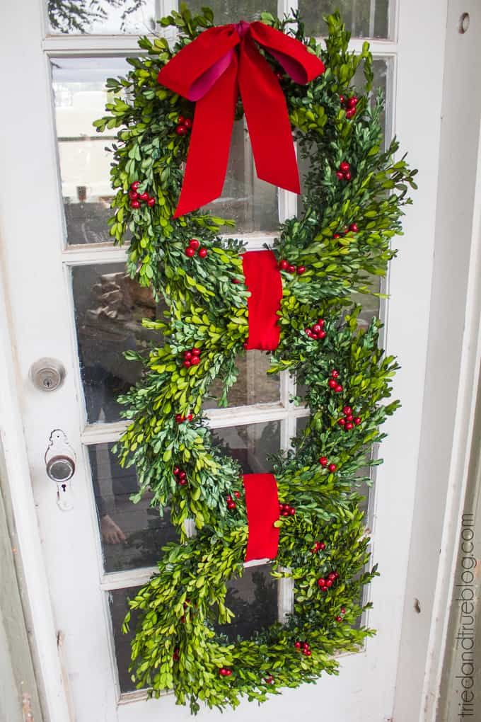 a christmas wreath hanging on the front door with red bows and holly berry garlands