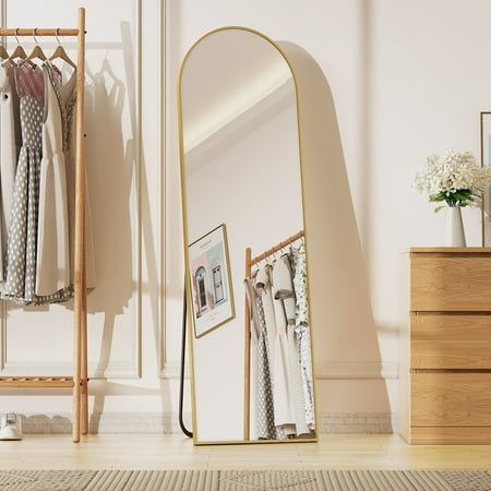 a mirror sitting on top of a wooden floor next to a dresser and clothes rack