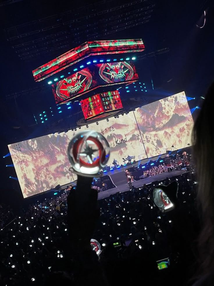 a person holding up a remote control in front of a large screen at a concert