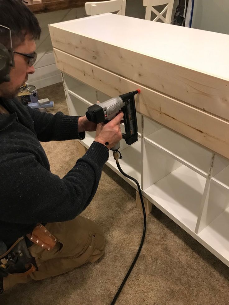 a man using a power drill to attach a piece of wood on top of a shelf