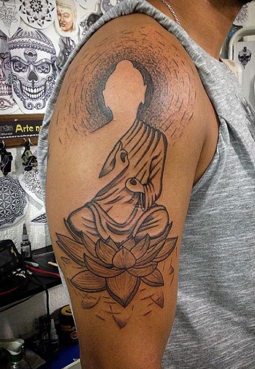 a man with a buddha tattoo on his arm and shoulder, holding a lotus flower