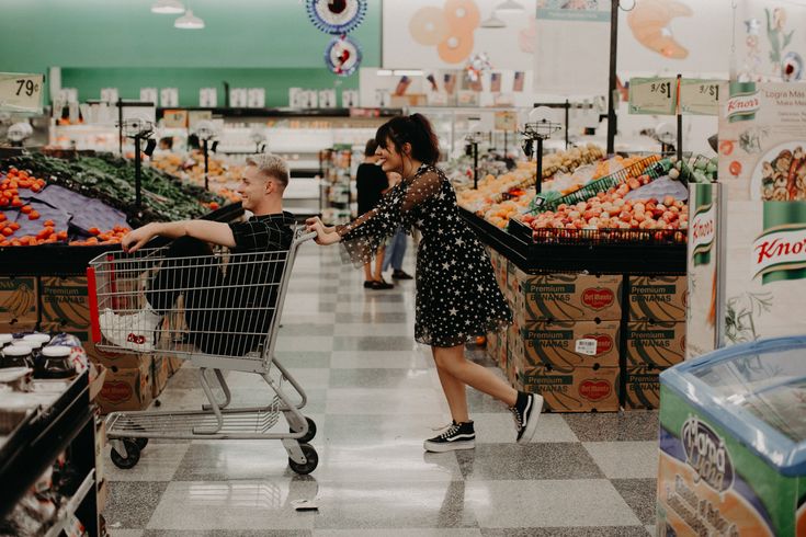 a woman pushing a shopping cart through a grocery store with a man in the background