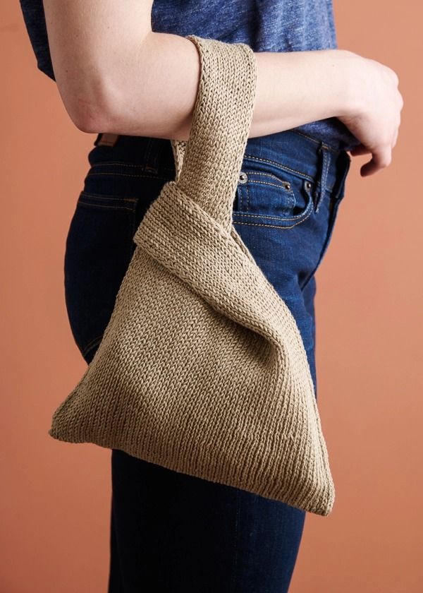 a woman is holding a knitted bag in her right hand while wearing jeans and a blue t - shirt