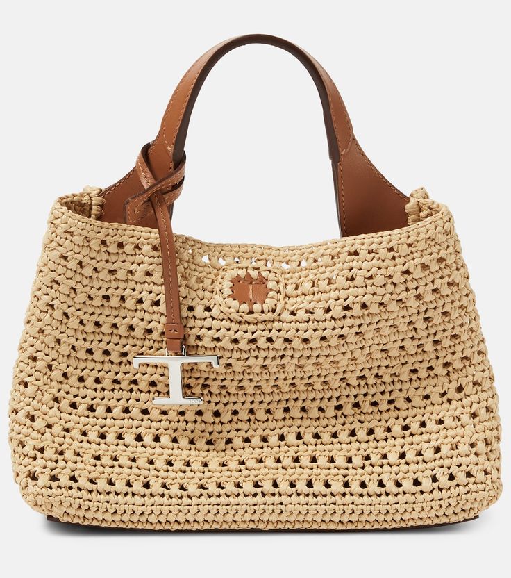 a crocheted straw bag with a cross on the front and brown leather handles