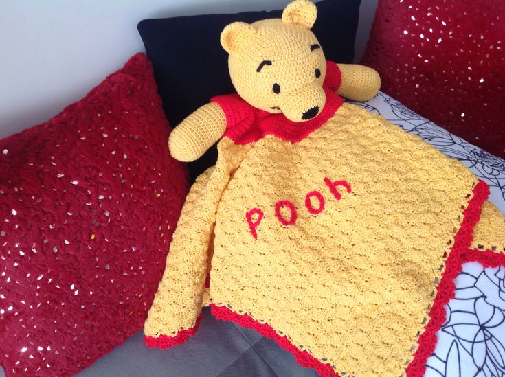 a crocheted pooh bear is laying on a bed with red and yellow pillows