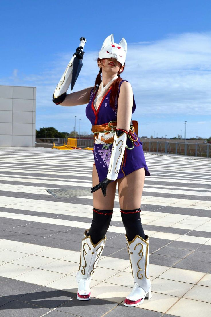 a woman dressed in costume standing on top of a cement floor with an umbrella over her head