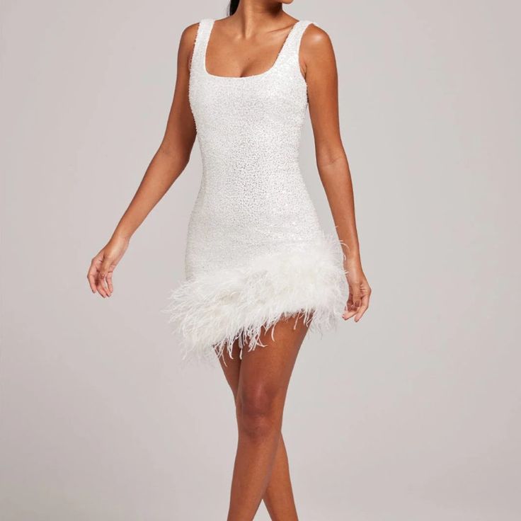 a woman in a short white dress with feathers on the skirt and heels standing up