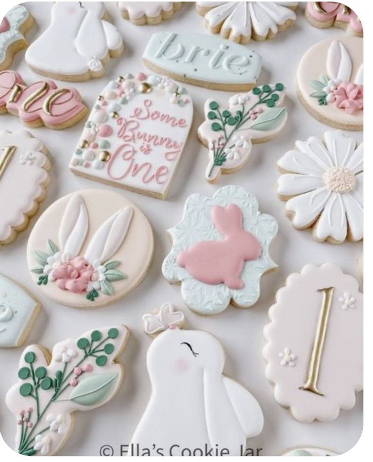 many decorated cookies are displayed on a white surface with pink and green accents, such as flowers, bunnies, bunny ears, and more