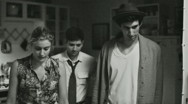 two men and a woman standing in a kitchen looking at something on the counter top