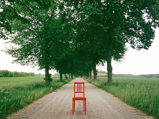 a red chair sitting in the middle of a dirt road