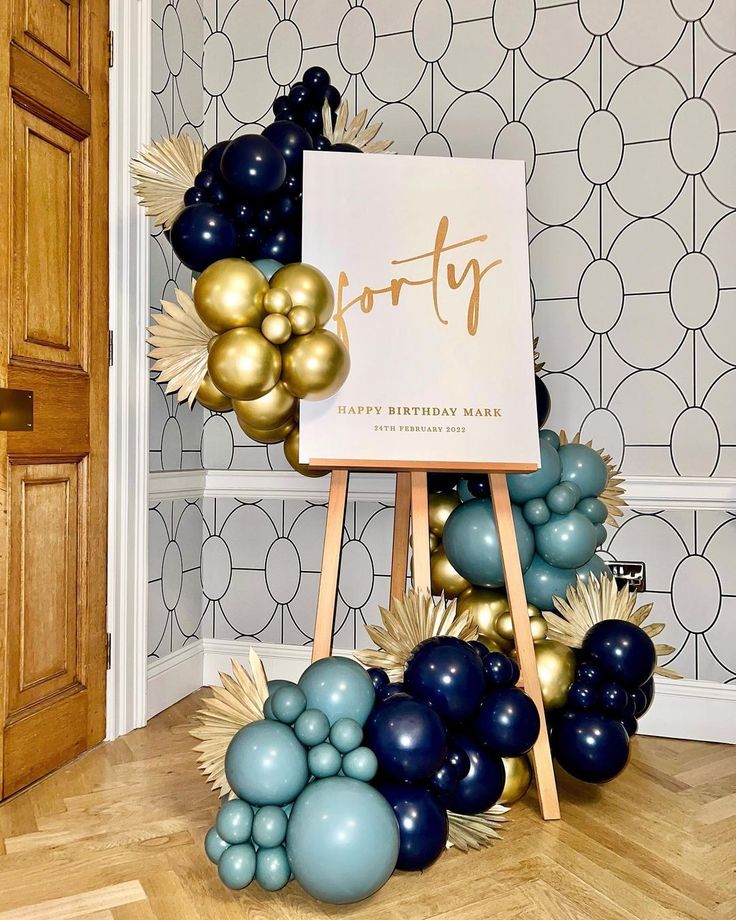 a birthday sign surrounded by balloons and gold foil stars on a wooden easel in front of a wallpapered background