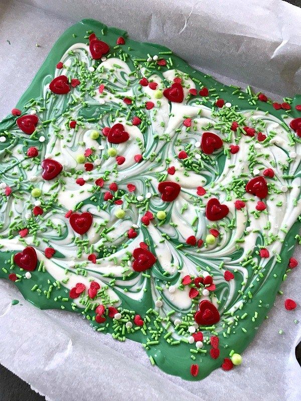 a green cake with white frosting and cherries on it, sitting in a paper wrapper