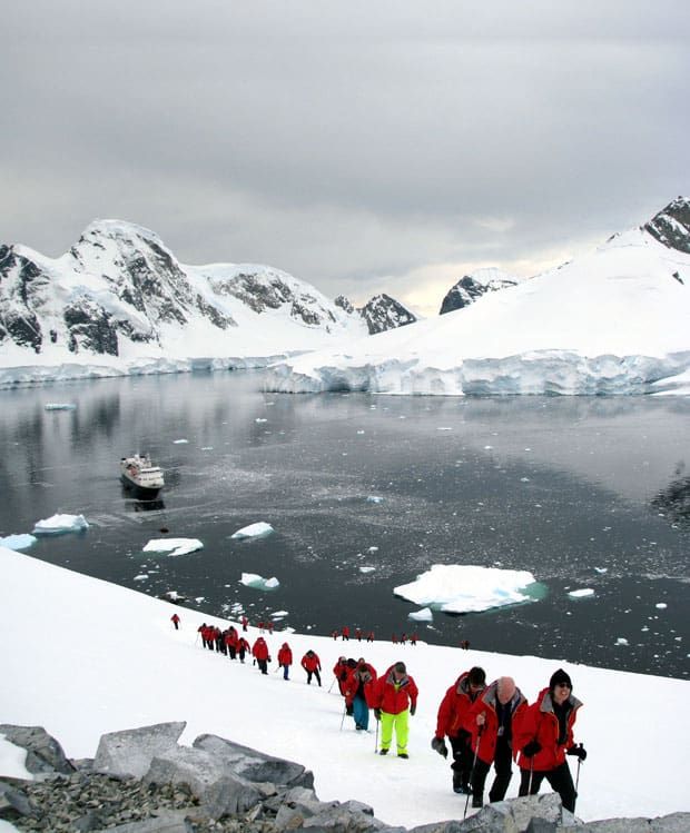 group of people in red jackets standing on snow covered ground next to water and icebergs