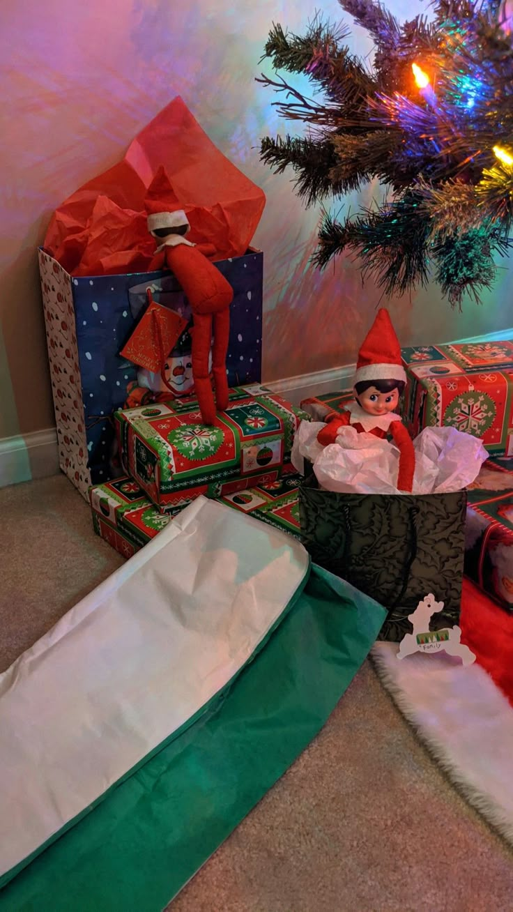 an elf sitting in a basket next to presents under a christmas tree on the floor