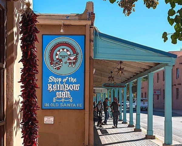 people are walking on the sidewalk near a building with a sign that says shop for the rainbow man in old santa fe