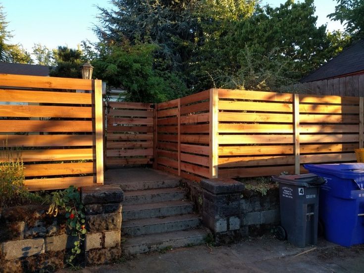 a wooden fence with steps leading up to it and trash cans in the foreground