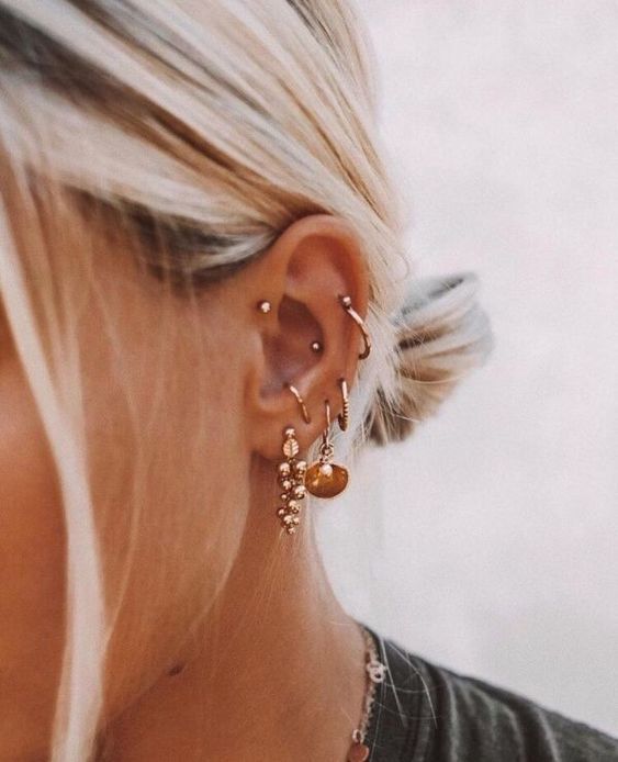 a woman with blonde hair wearing gold earrings and a black shirt is looking down at her ear