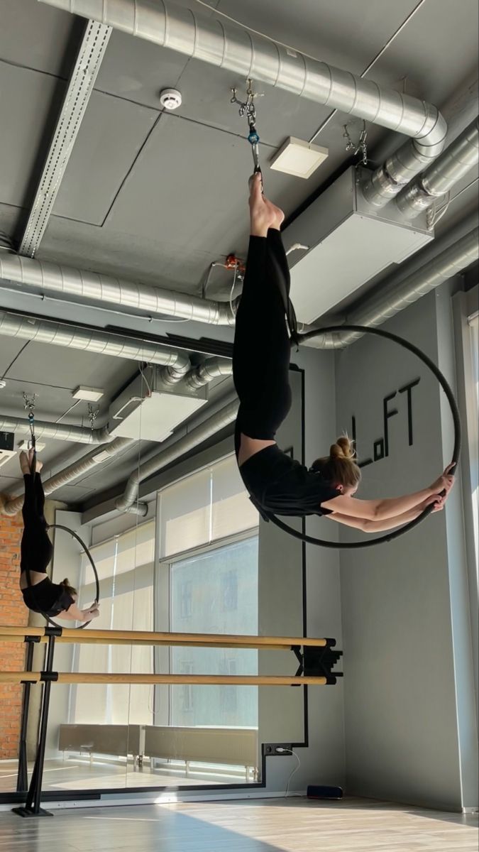 two women doing aerial acrobatic tricks in an office building, one on a hoop and the other upside down