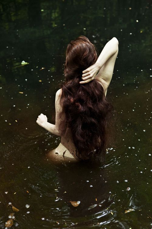 a woman is sitting in the water with her back turned to the camera and she has long dark hair