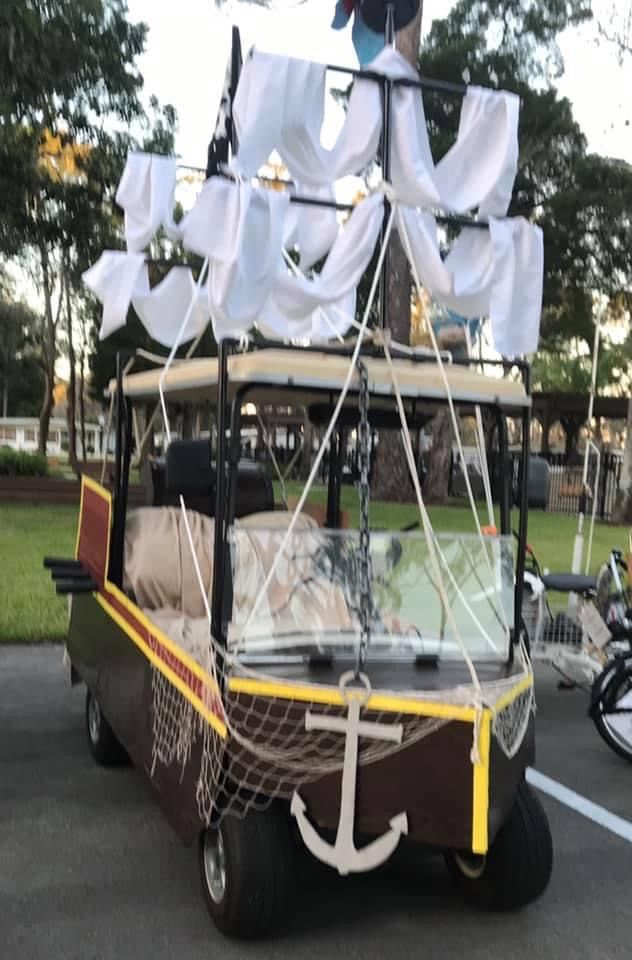 a golf cart with a sailboat on the back is parked in a parking lot