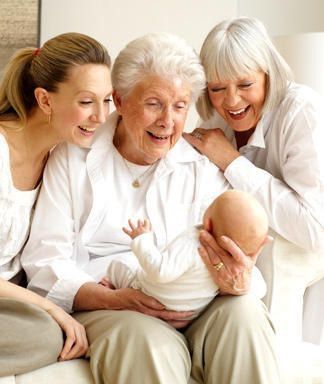 an older woman and two younger women holding a baby in her lap while sitting on a couch