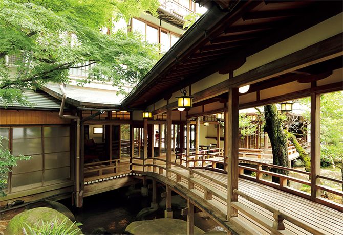 a wooden bridge over a small stream in front of a building with lots of windows