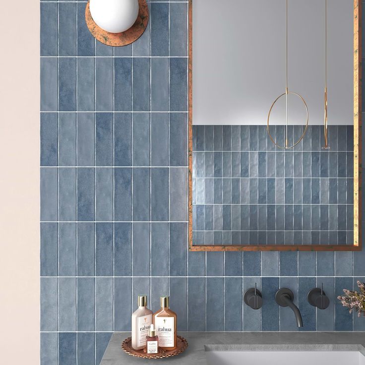 a bathroom with blue tiles on the wall and a mirror above it, next to a sink