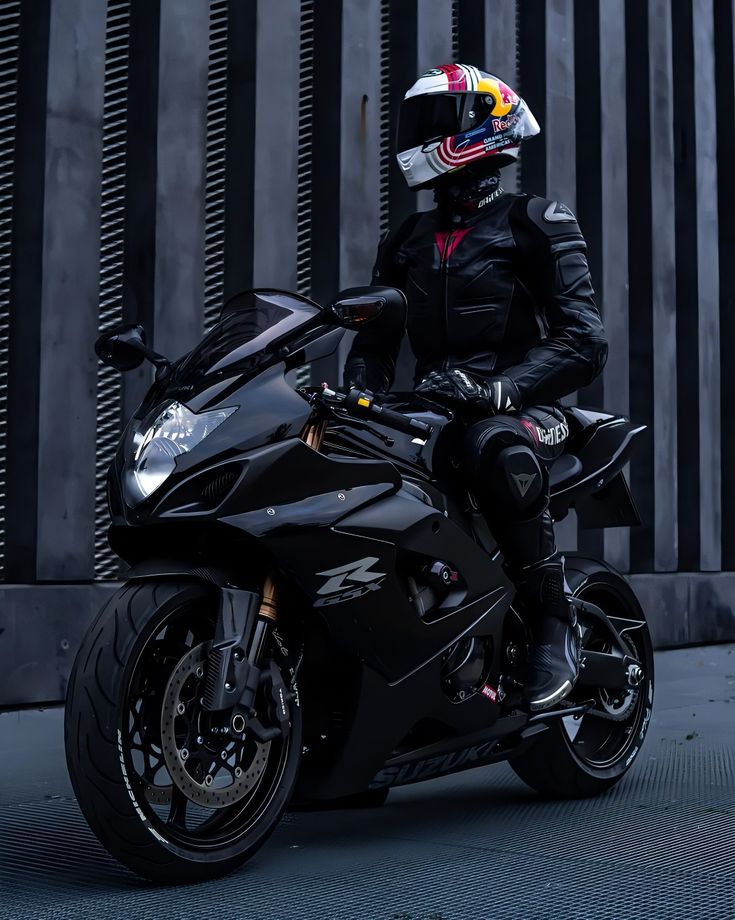 a man sitting on the back of a black motorcycle wearing a helmet and leather outfit