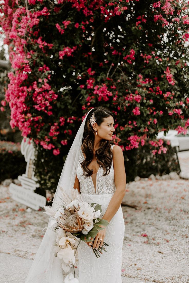 a woman in a wedding dress standing next to a tree with pink flowers on it