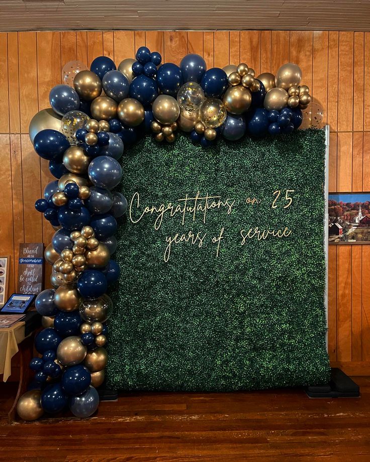 a green and gold backdrop with congratulations written on the side, surrounded by blue and gold balloons