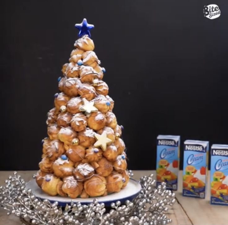 a small christmas tree made out of rolls and other pastries on a table next to boxes of krispy kreme