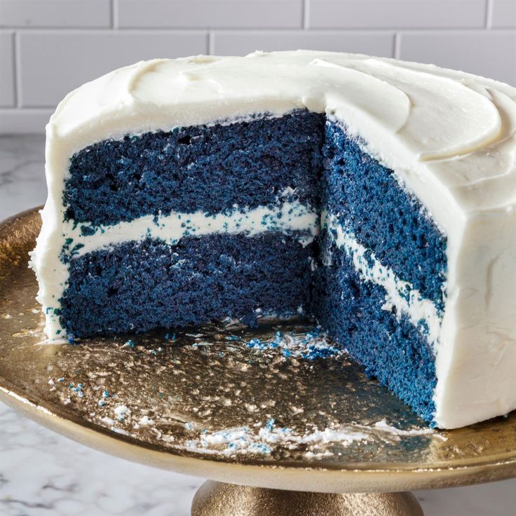 a blue cake with white frosting is on a gold platter and has one slice cut out