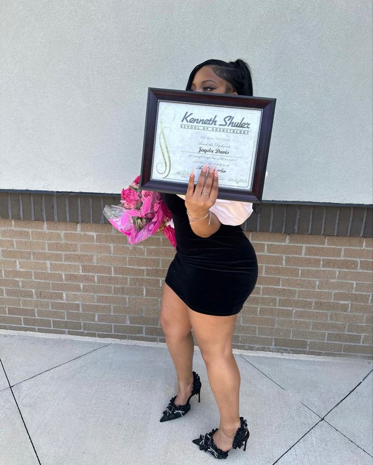 a woman in black dress holding up a framed plaque with pink flowers on it's chest