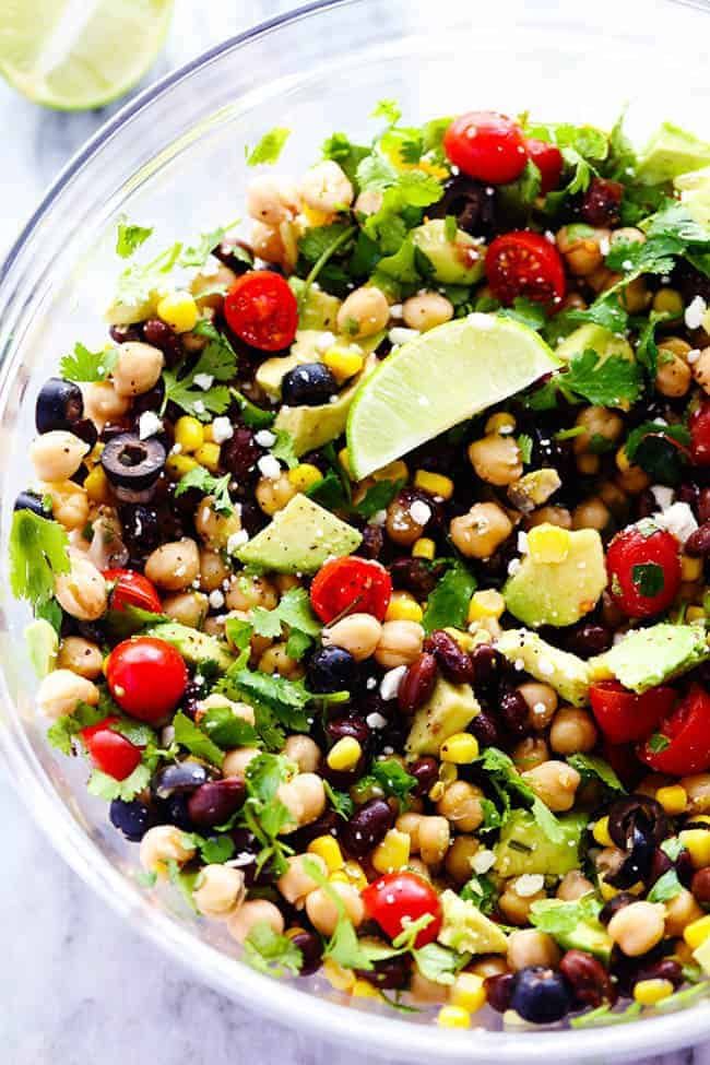 a salad in a glass bowl with avocado, tomatoes, black beans, corn and cilantro