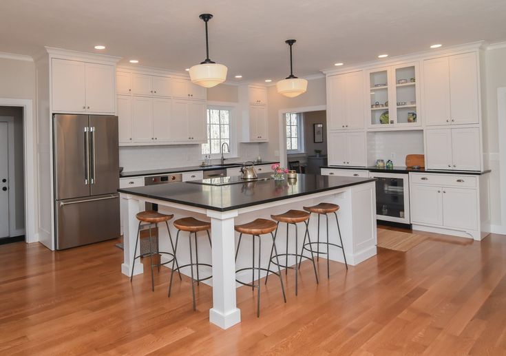 a large kitchen with white cabinets and black counter tops, an island in the middle is surrounded by four stools