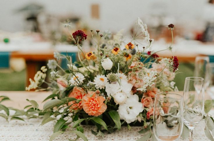 an arrangement of flowers and greenery on a table with wine glasses, napkins and plates