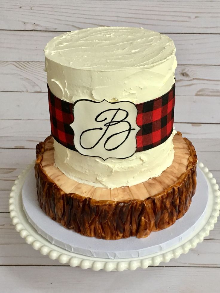 a white cake topped with a red and black plaid ribbon on top of a wooden slice