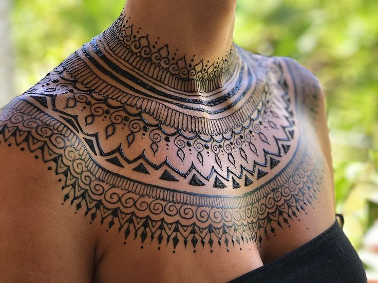 a woman's chest with an intricate tattoo design on her upper half and neck