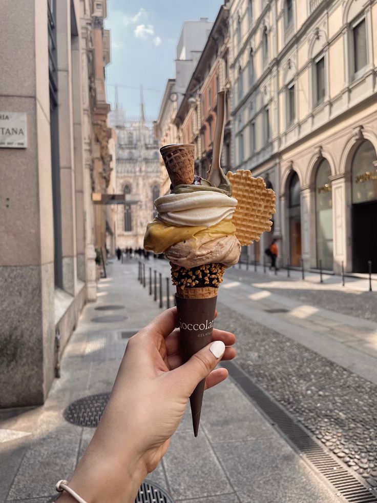 a person holding up an ice cream cone in the middle of a street with buildings on both sides