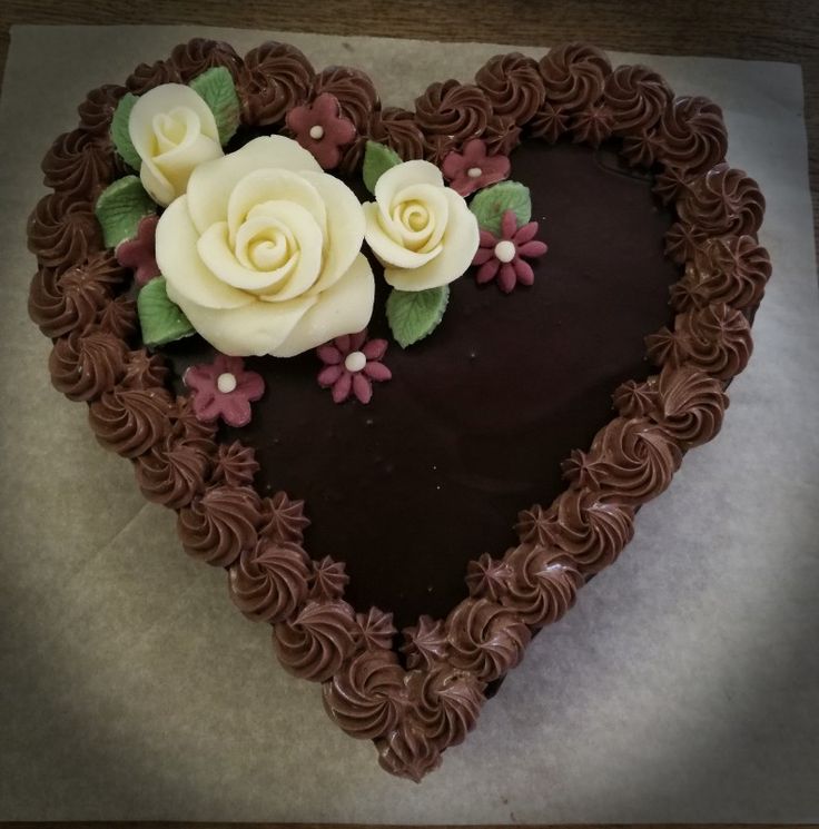 a heart shaped cake with chocolate frosting and white roses on the top is shown