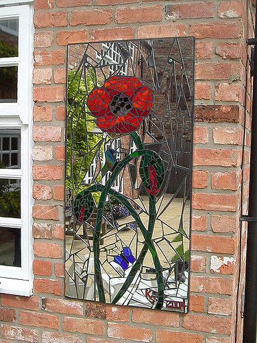 a stained glass window on the side of a brick building with red flowers in it