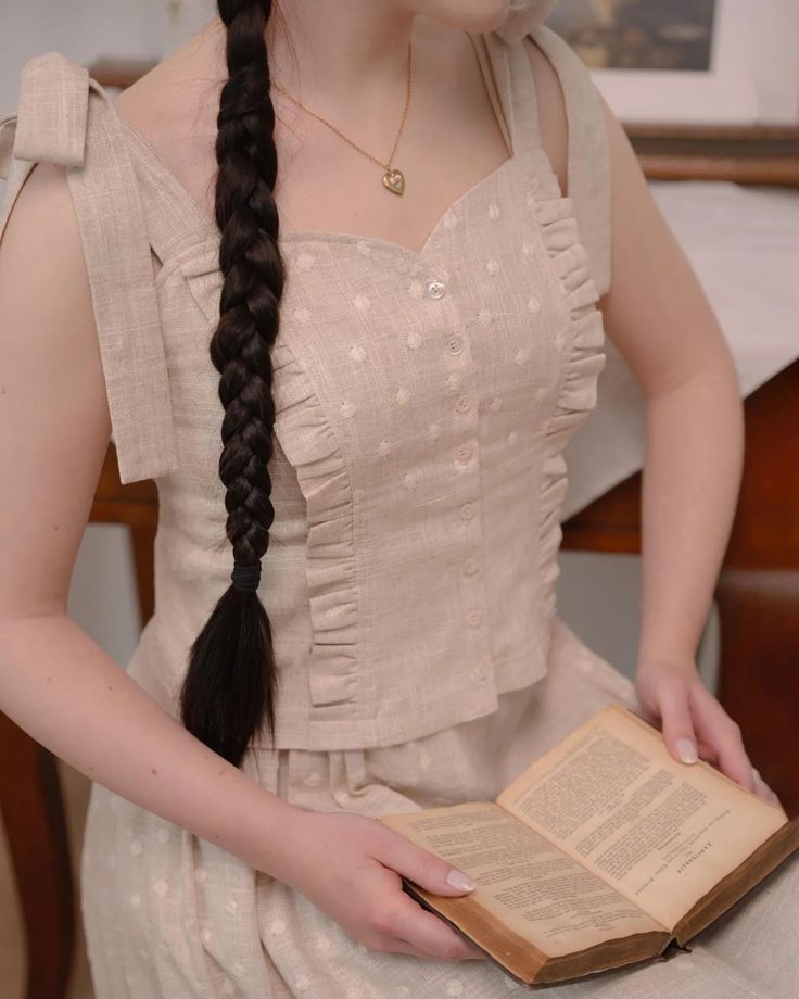 a woman with long hair sitting down holding an open book in her hands and looking at the camera