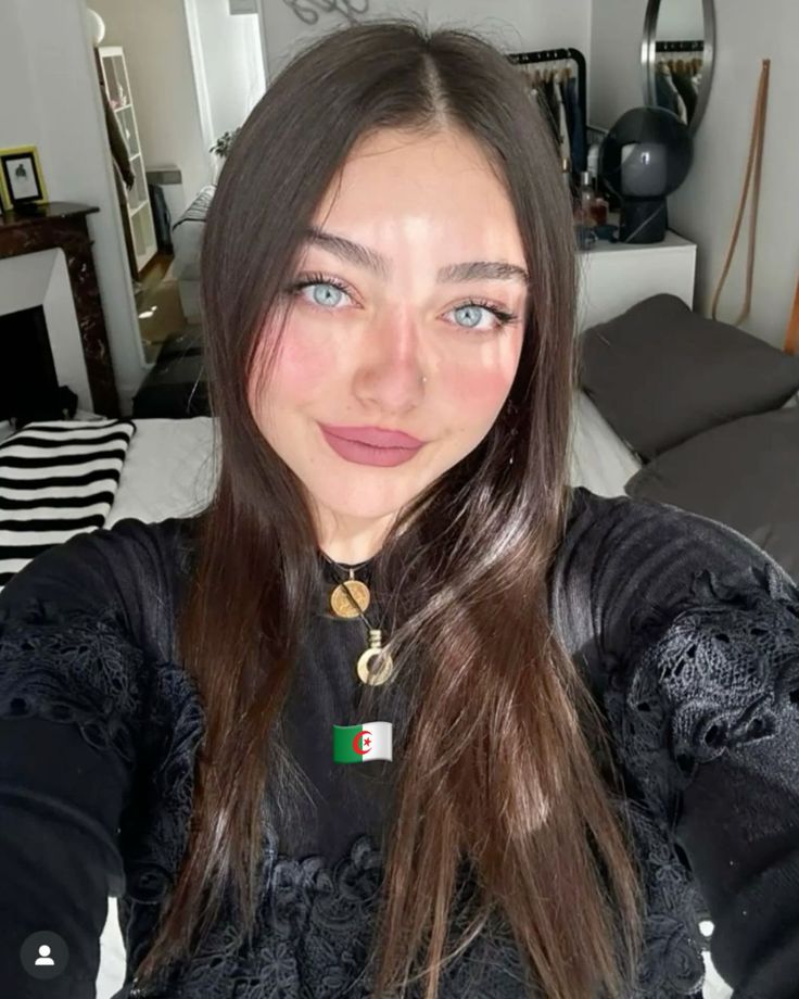 a woman with long brown hair wearing a black shirt and gold necklace is taking a selfie