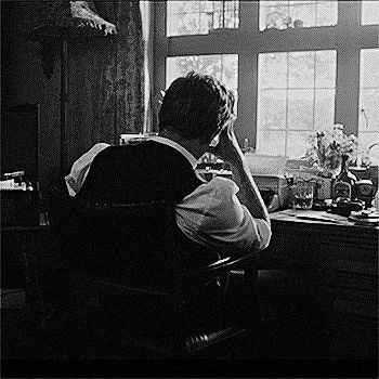 a man sitting at a desk in front of a window with his hands on his head